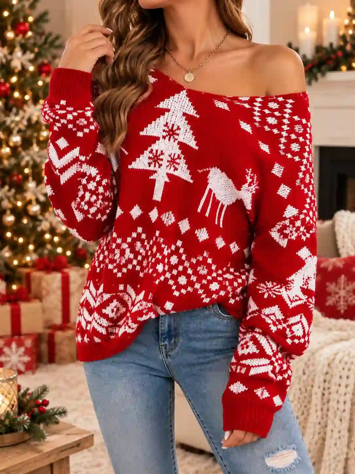 A woman wearing a festive red and white Christmas knit sweater with a deer and tree pattern, paired with blue jeans, in a cozy holiday living room setting.
